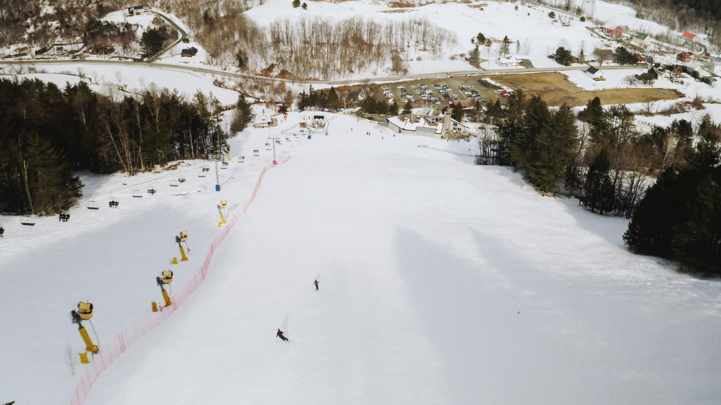Ski slope with skiers, surrounded by snow-covered trees and buildings.