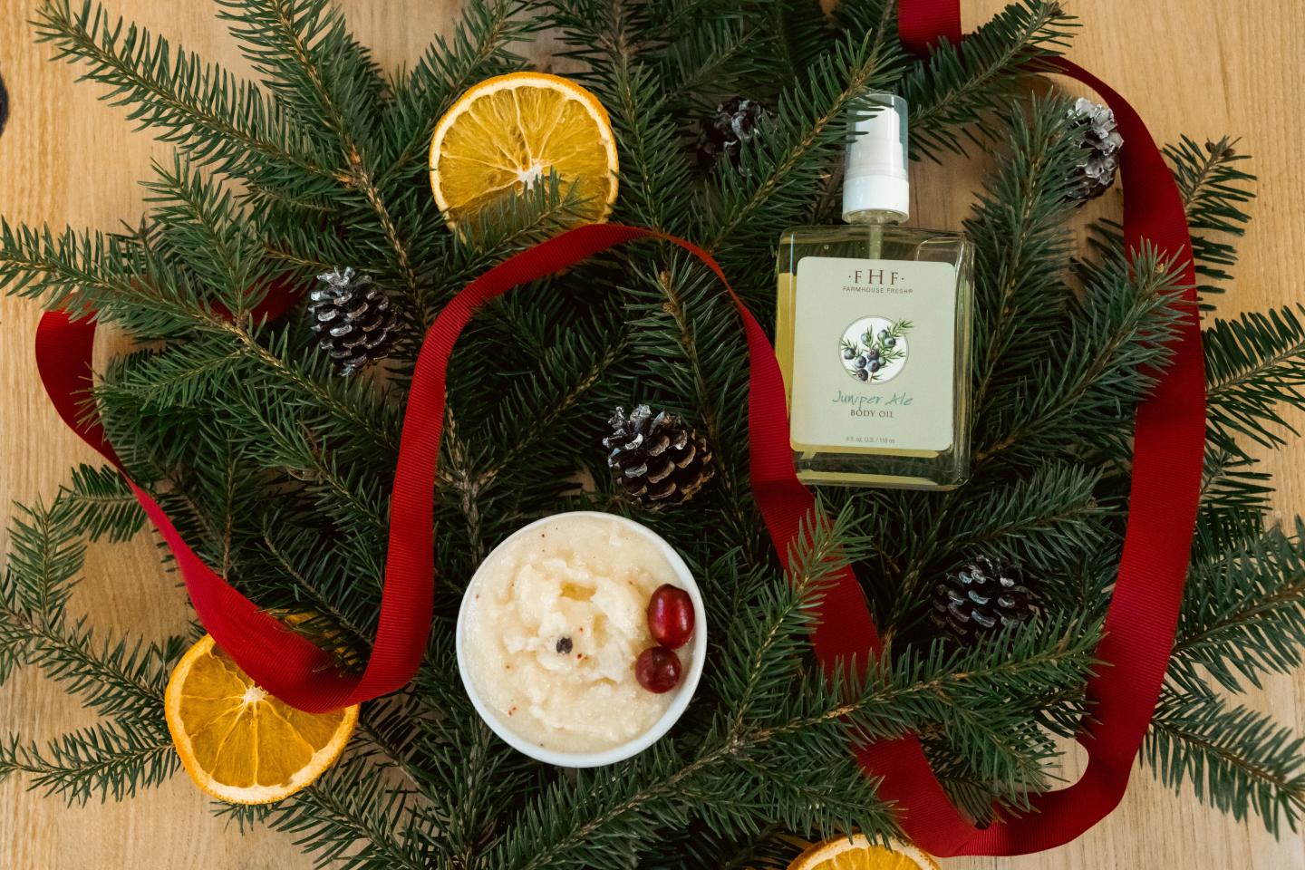 Evergreen sprigs with red ribbon, orange slices, pinecones, cream, and bottled perfume.