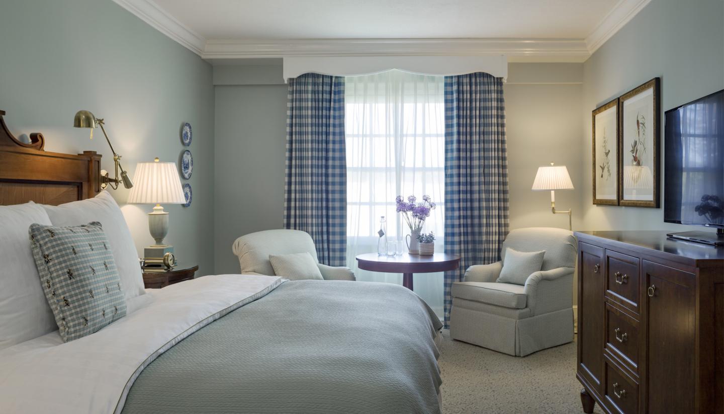 Cozy hotel room with a bed, armchair, and window with checkered curtains.