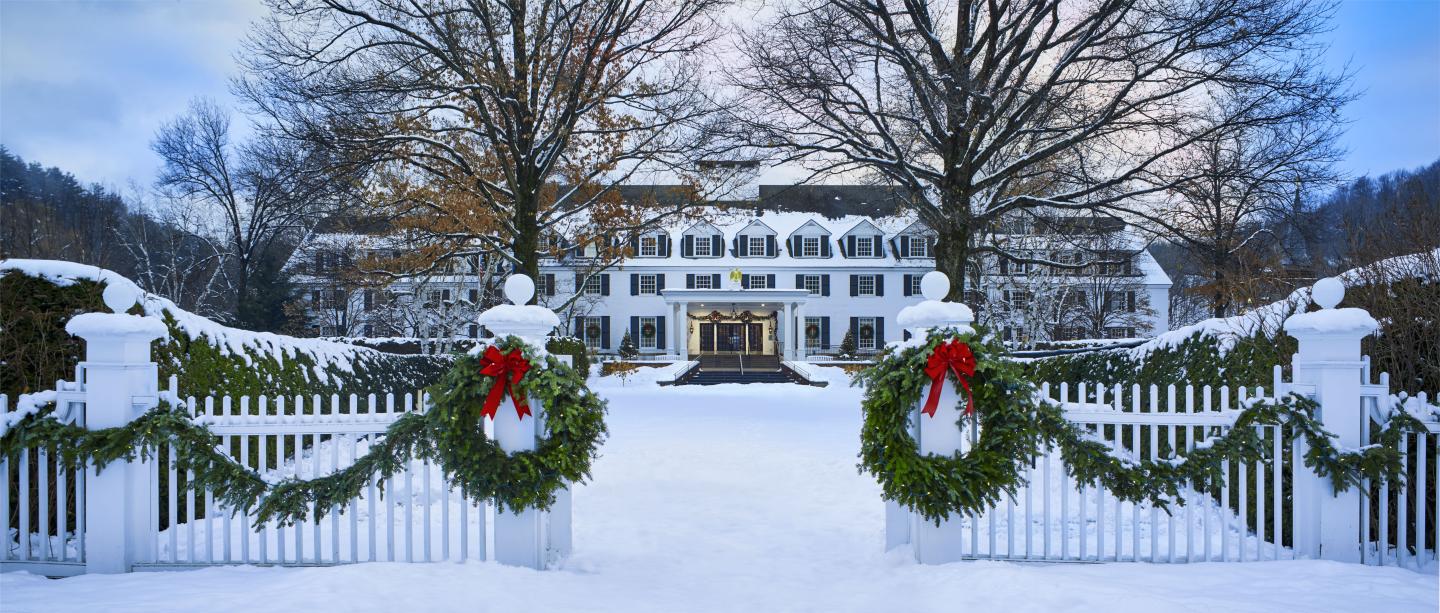 Snow-covered entrance to a white colonial building with wreaths on the gate.