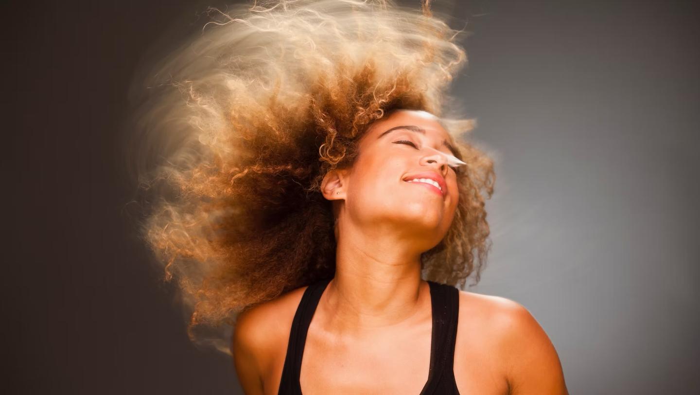 Smiling woman with curly hair backlit, head tossed to the side.