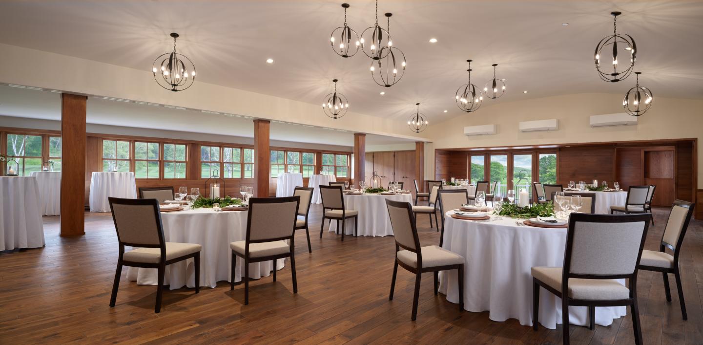 Bright banquet hall, round tables with white tablecloths, elegant chairs, decorative lights.
