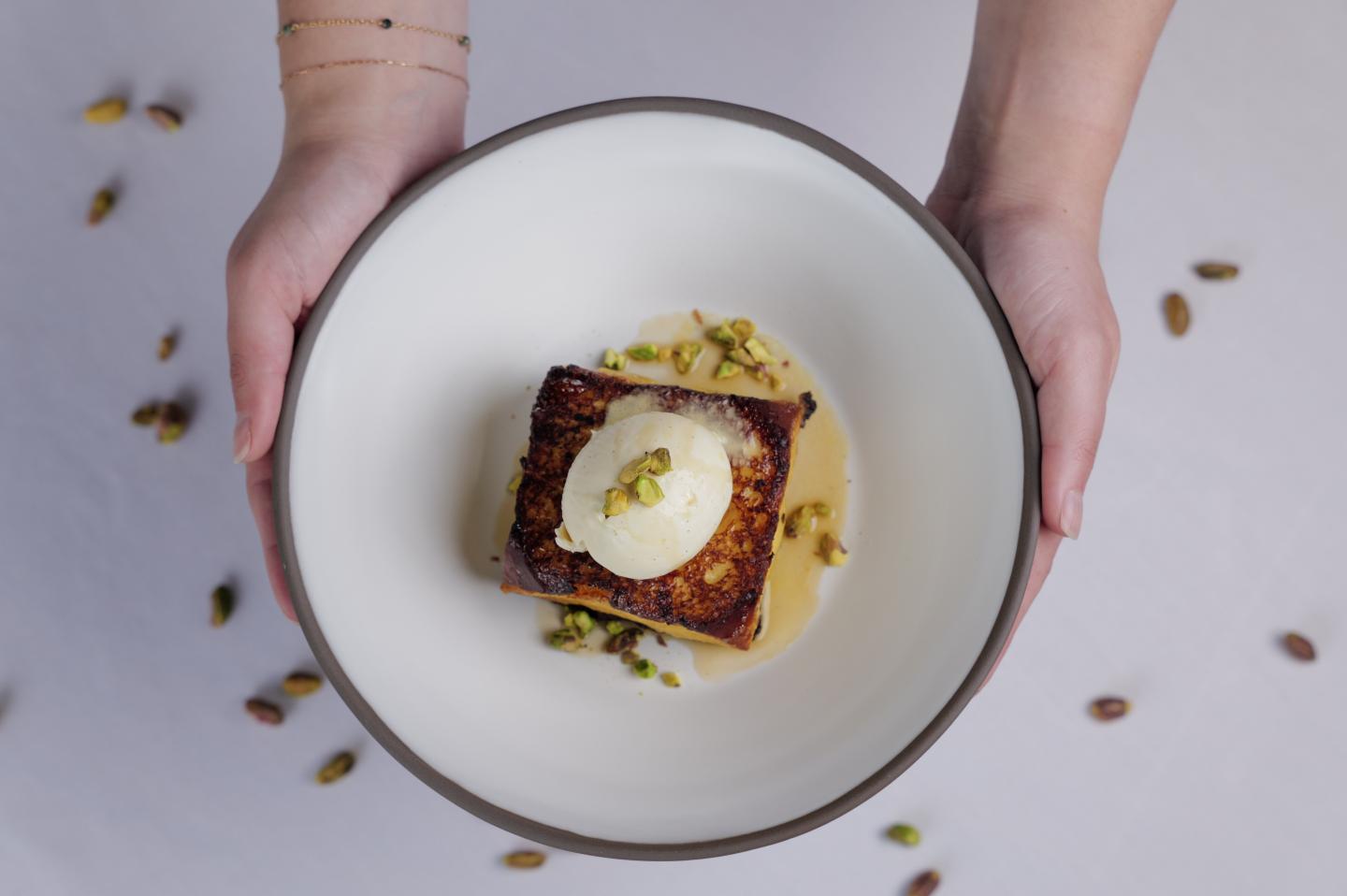 Dessert with ice cream and pistachios on a plate held by two hands.