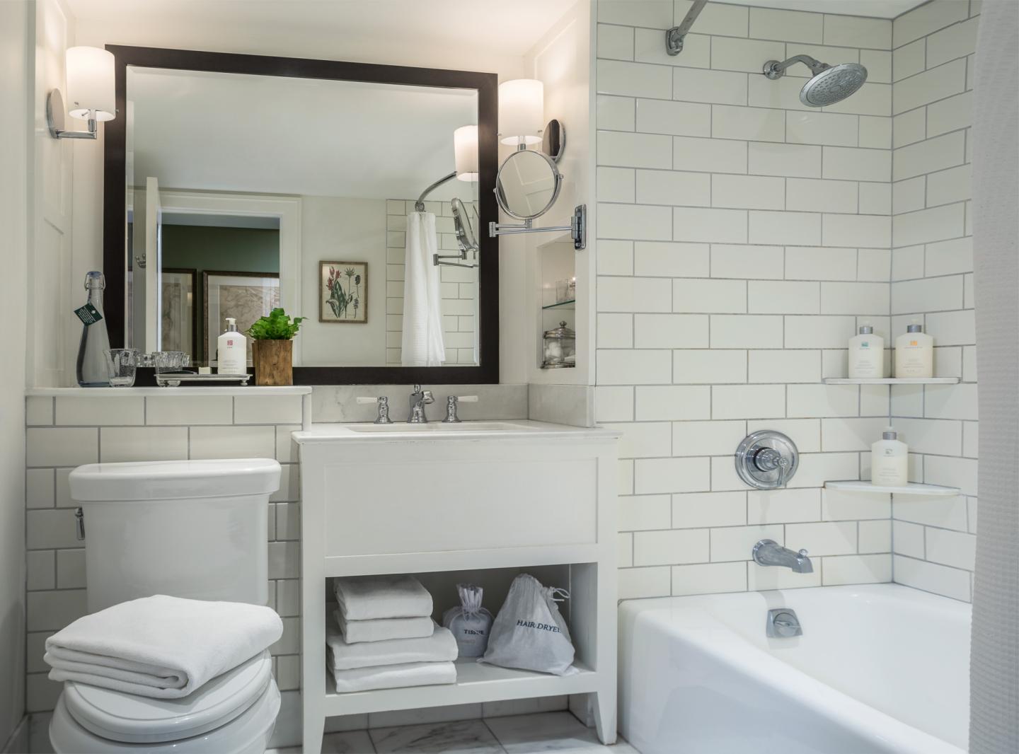 Bathroom with white tiles, vanity, mirror, and bathtub.