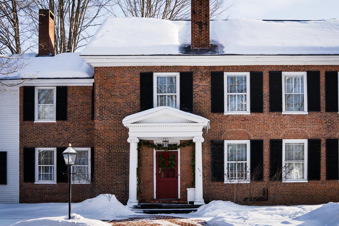 Brick house with red door, black shutters, and snow-covered roof.