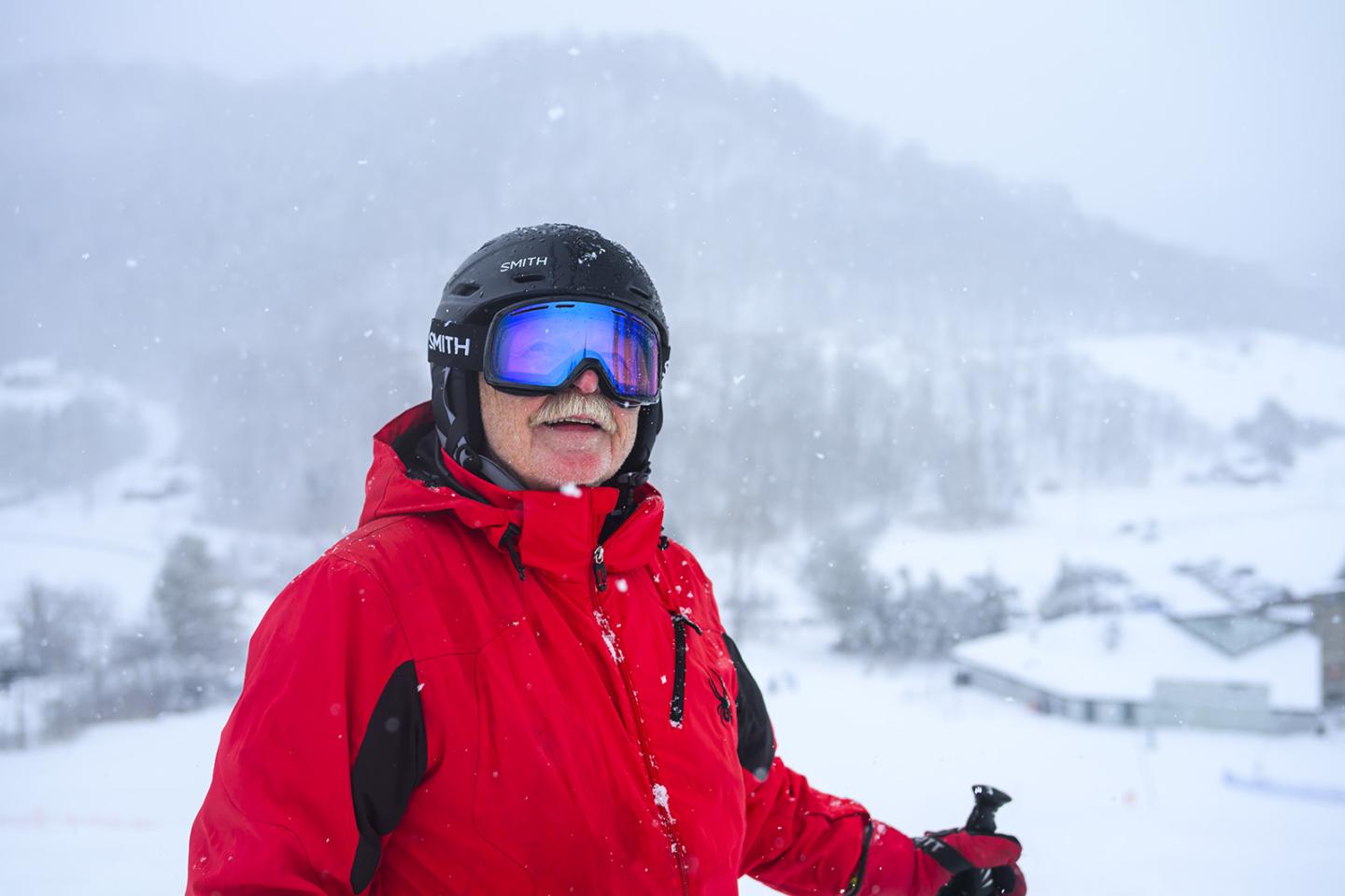 Senior Skier in red jacket with goggles on snowy mountain.