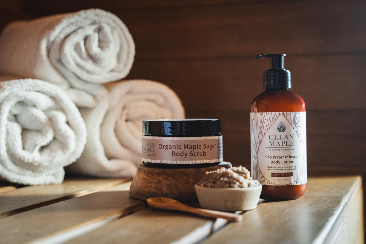 Maple sugar scrub, lotion, and towels on wooden surface.