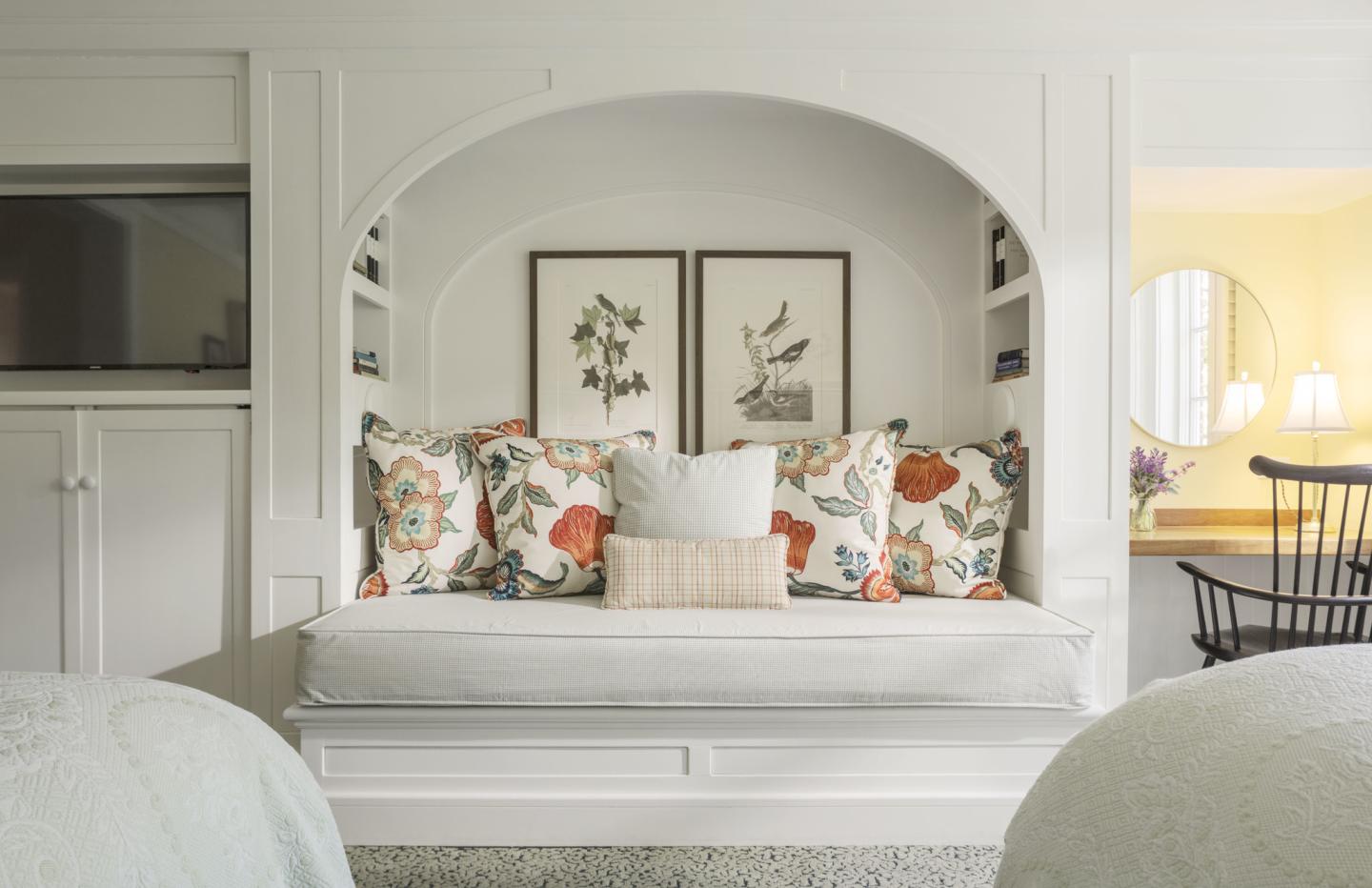 Cozy nook with floral pillows, framed bird art, and warm lighting.