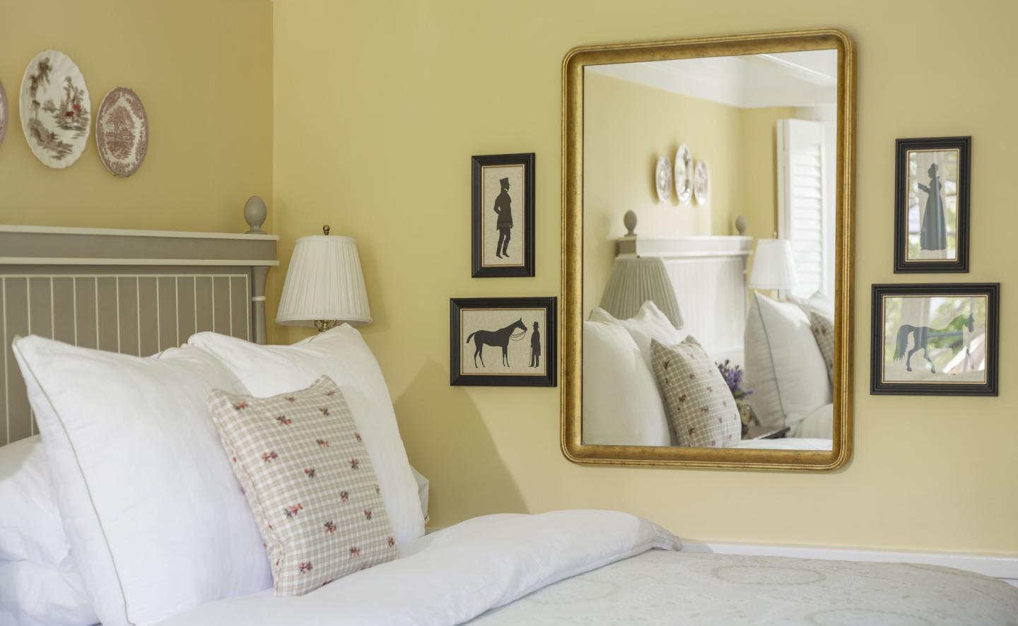 Cozy bedroom with white bedding, framed mirror, and yellow walls.