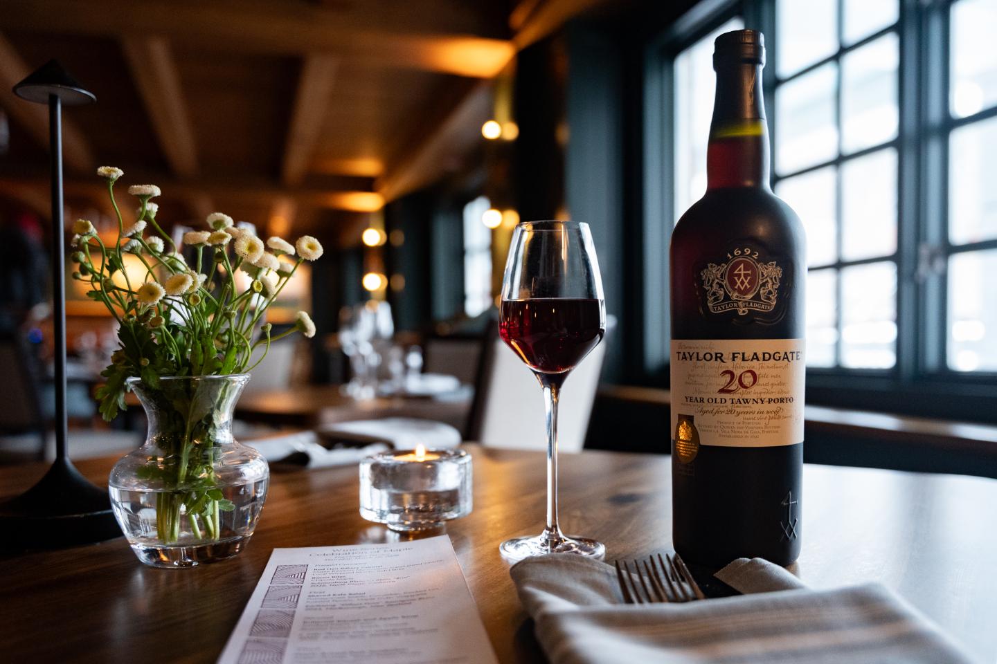 Cozy restaurant, wine bottle and glass on table, vase of flowers nearby.