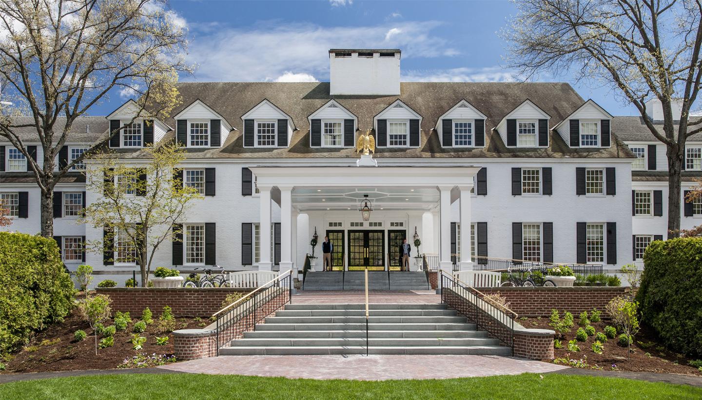 Grand white building with a sloping roof, black shutters, and a manicured lawn.