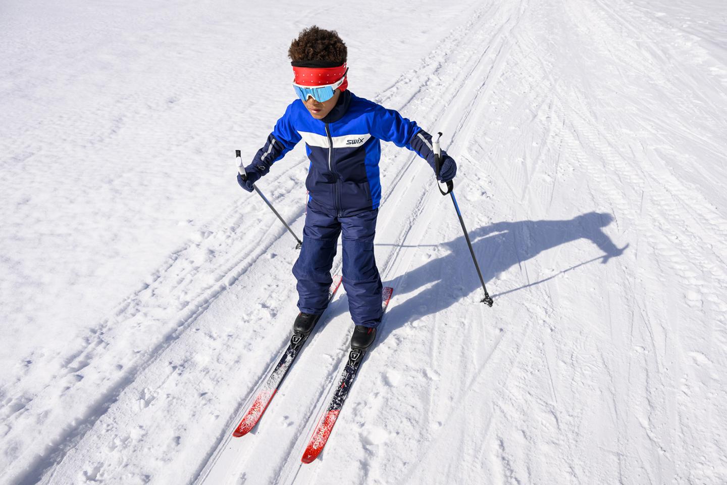 Young nordic skier in blue gear glides on snowy trail on a sunny day.