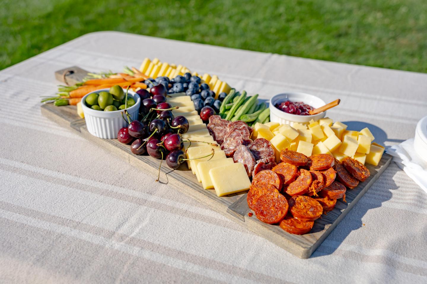 Charcuterie board with meats, cheeses, fruits, and vegetables outdoors.