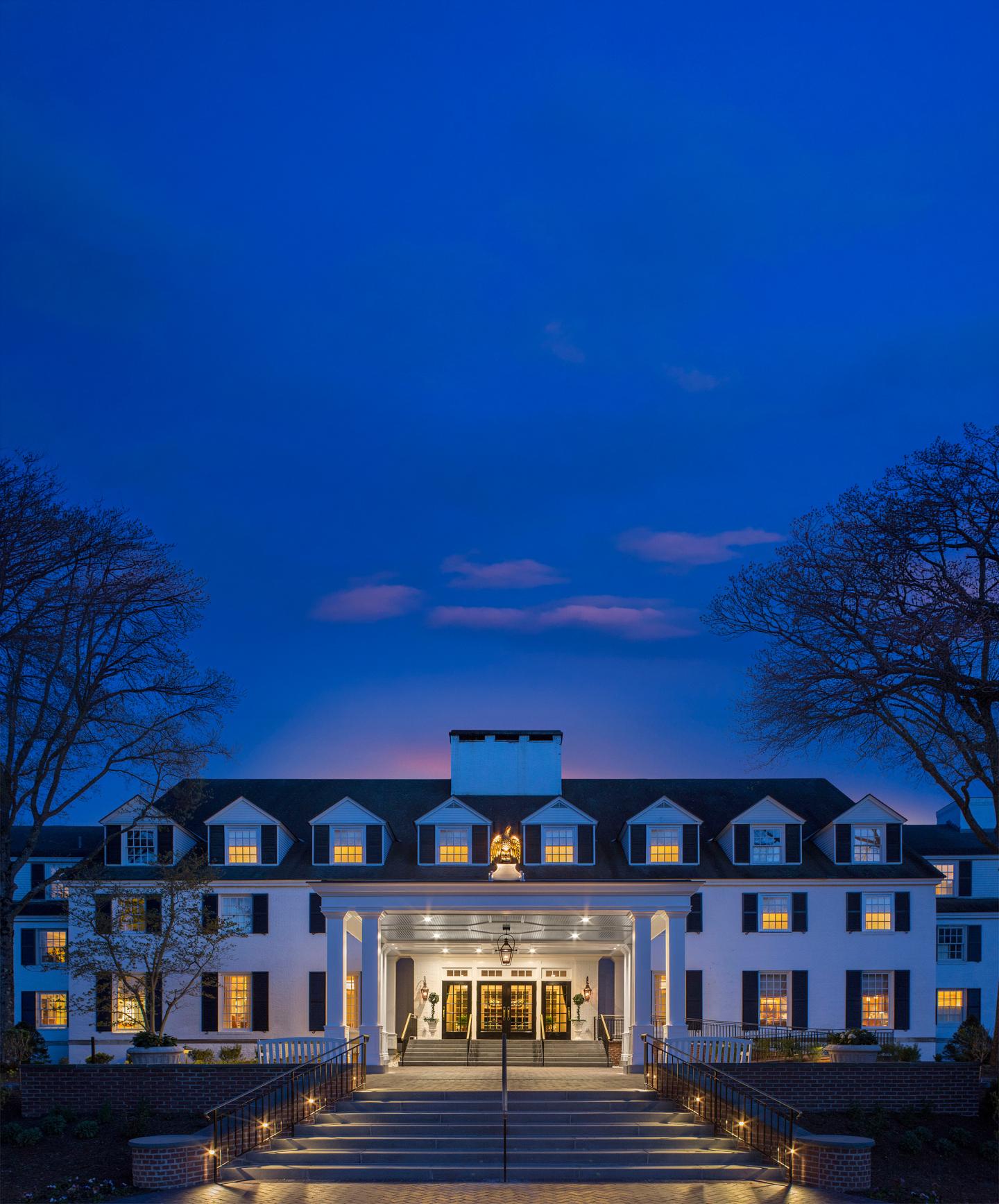 Grand hotel entrance at dusk with lit windows, framed by trees.