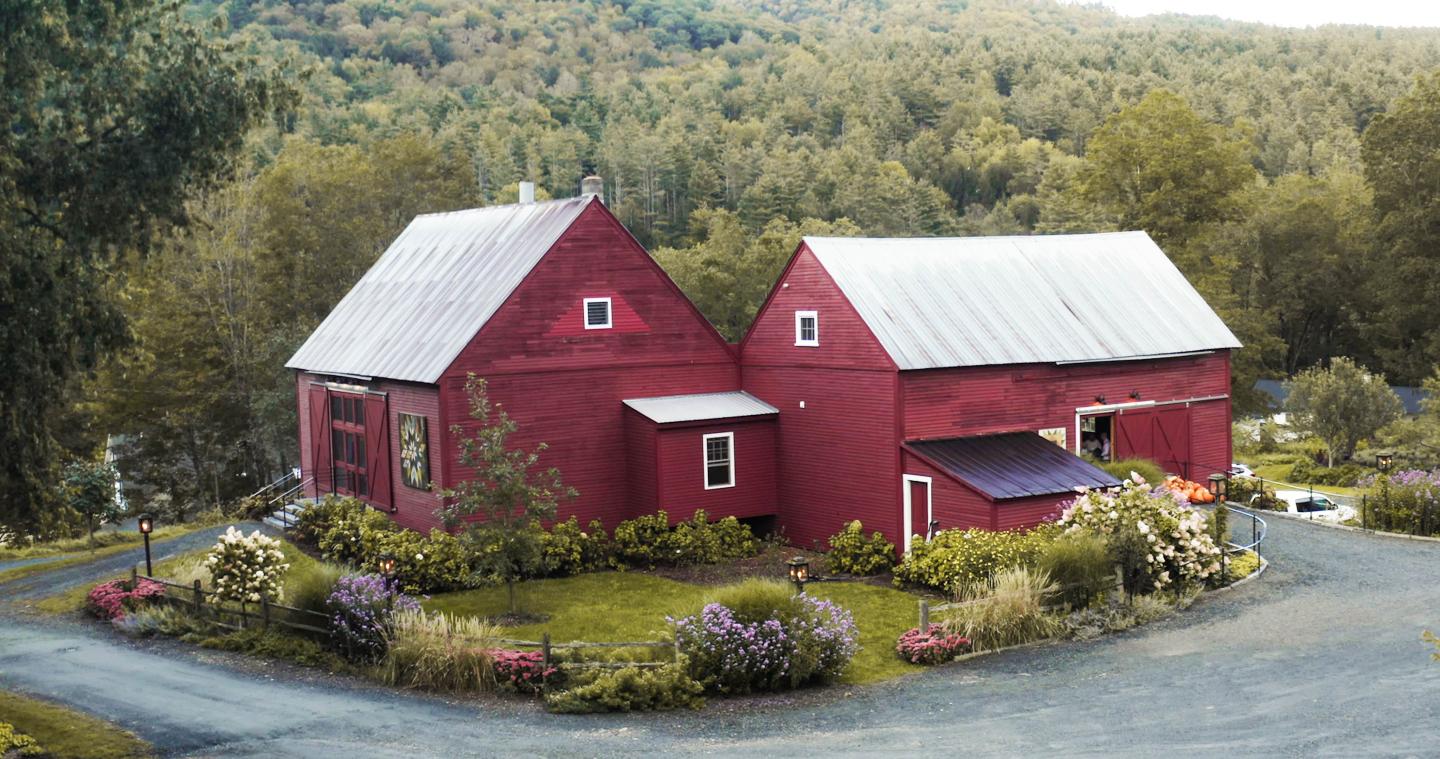 Red barn and house surrounded by colorful garden and trees.