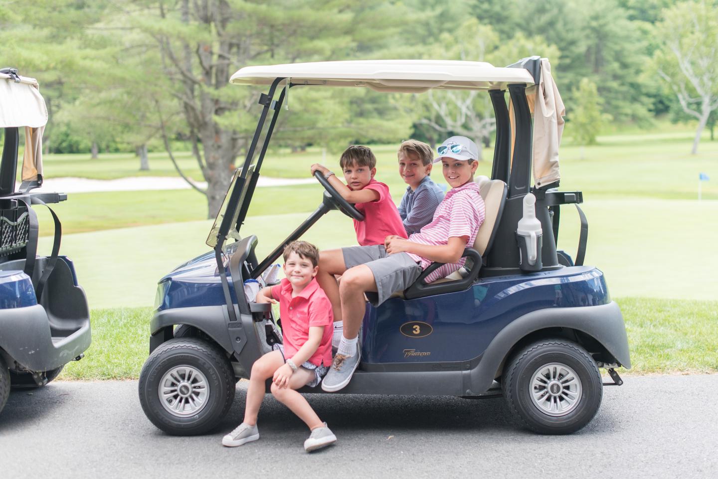 Family smiling in a golf cart on a sunny day.