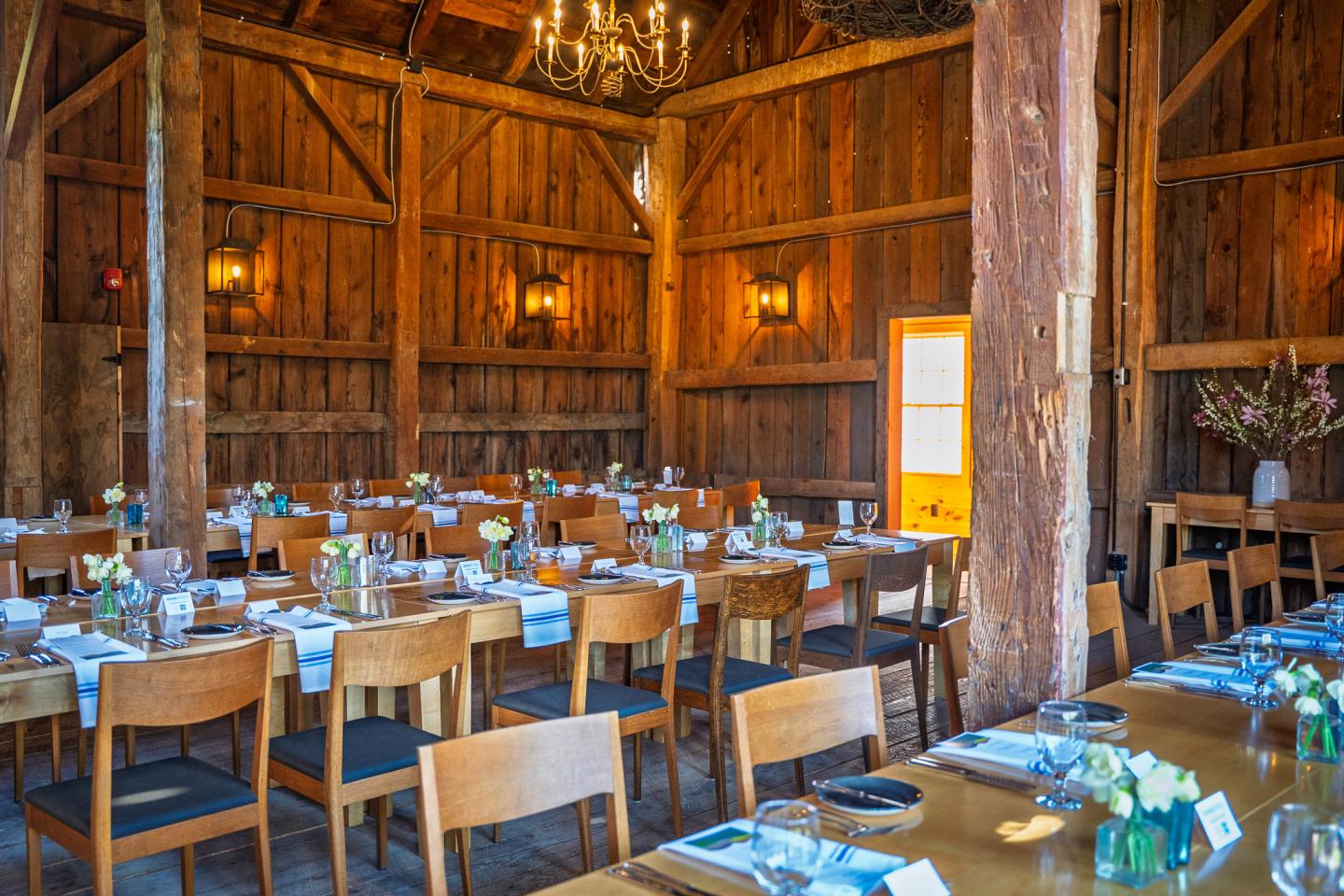 Rustic dining hall with wooden tables, chairs, and dim chandeliers.