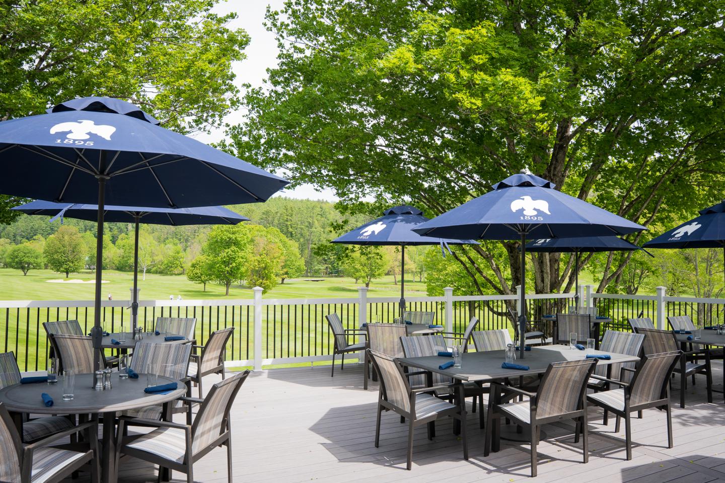 Outdoor patio with tables, chairs, and blue umbrellas under sunny skies.