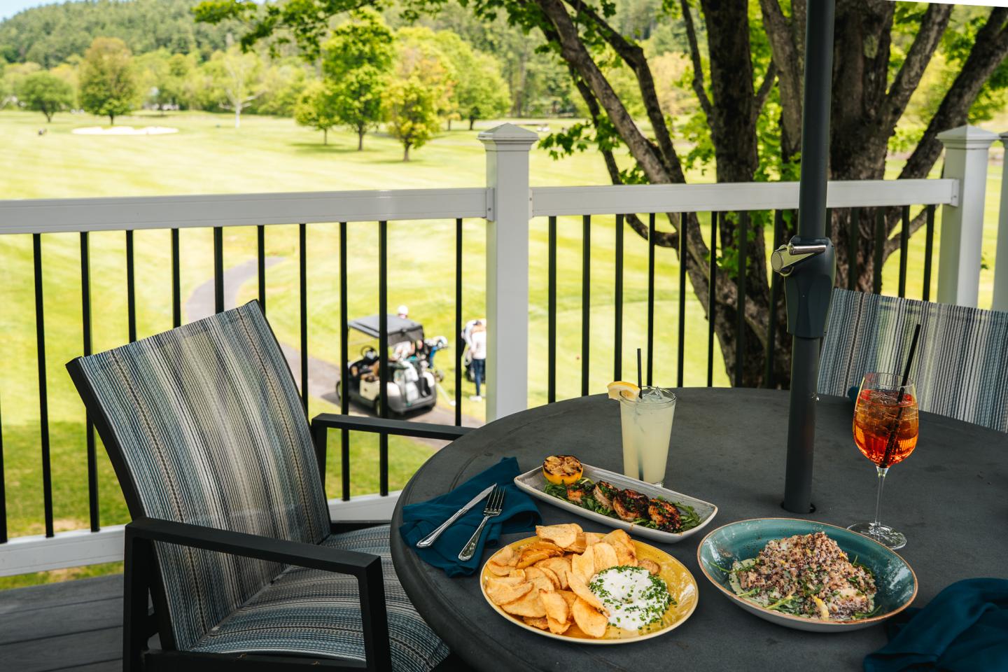 Deck dining with chips, salad, drinks; view of golf course and trees.