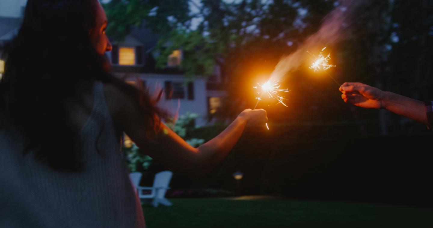Two people holding sparklers in a garden at dusk.