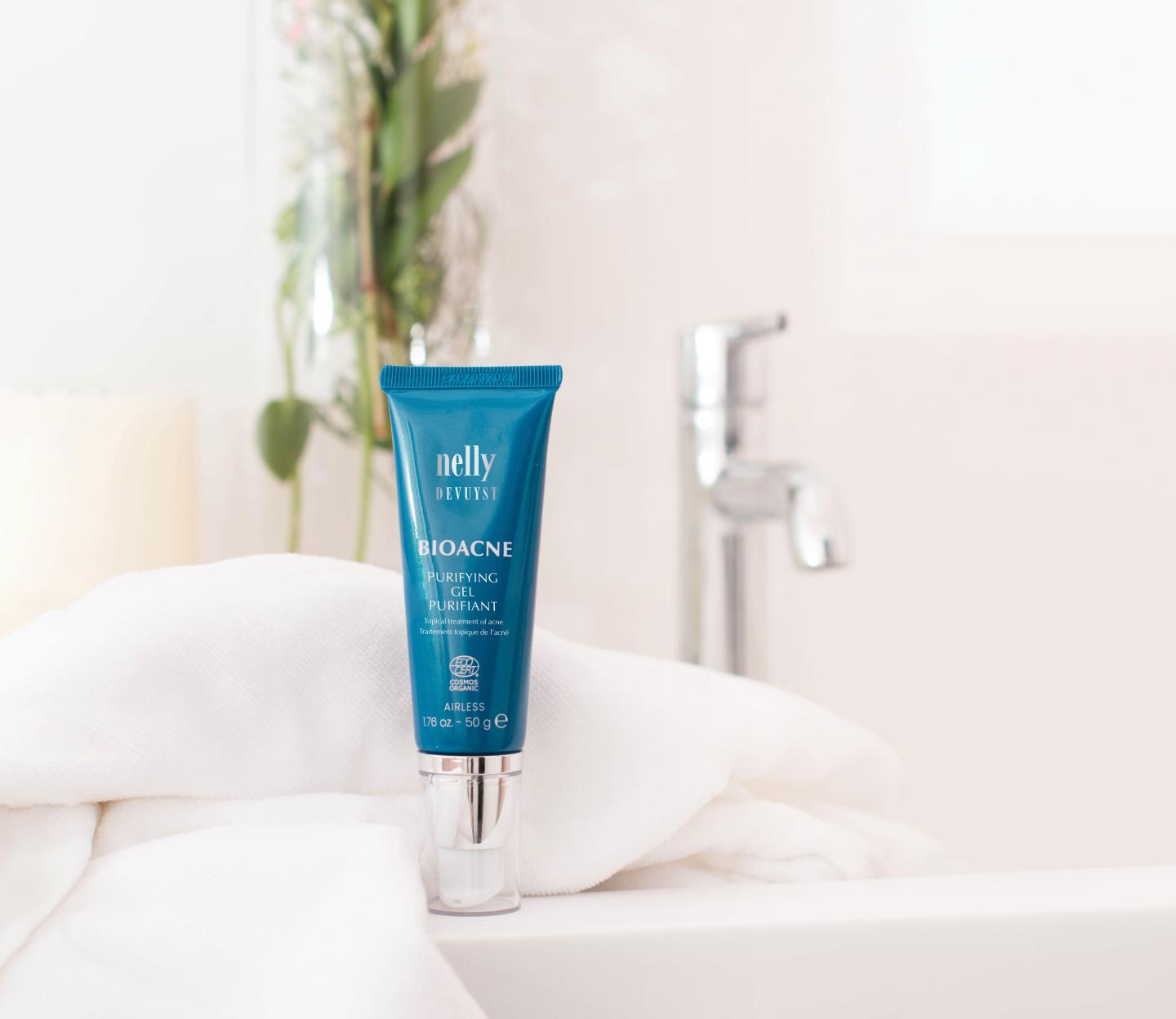 Blue cosmetic tube on a white towel beside a faucet in a bathroom setting.