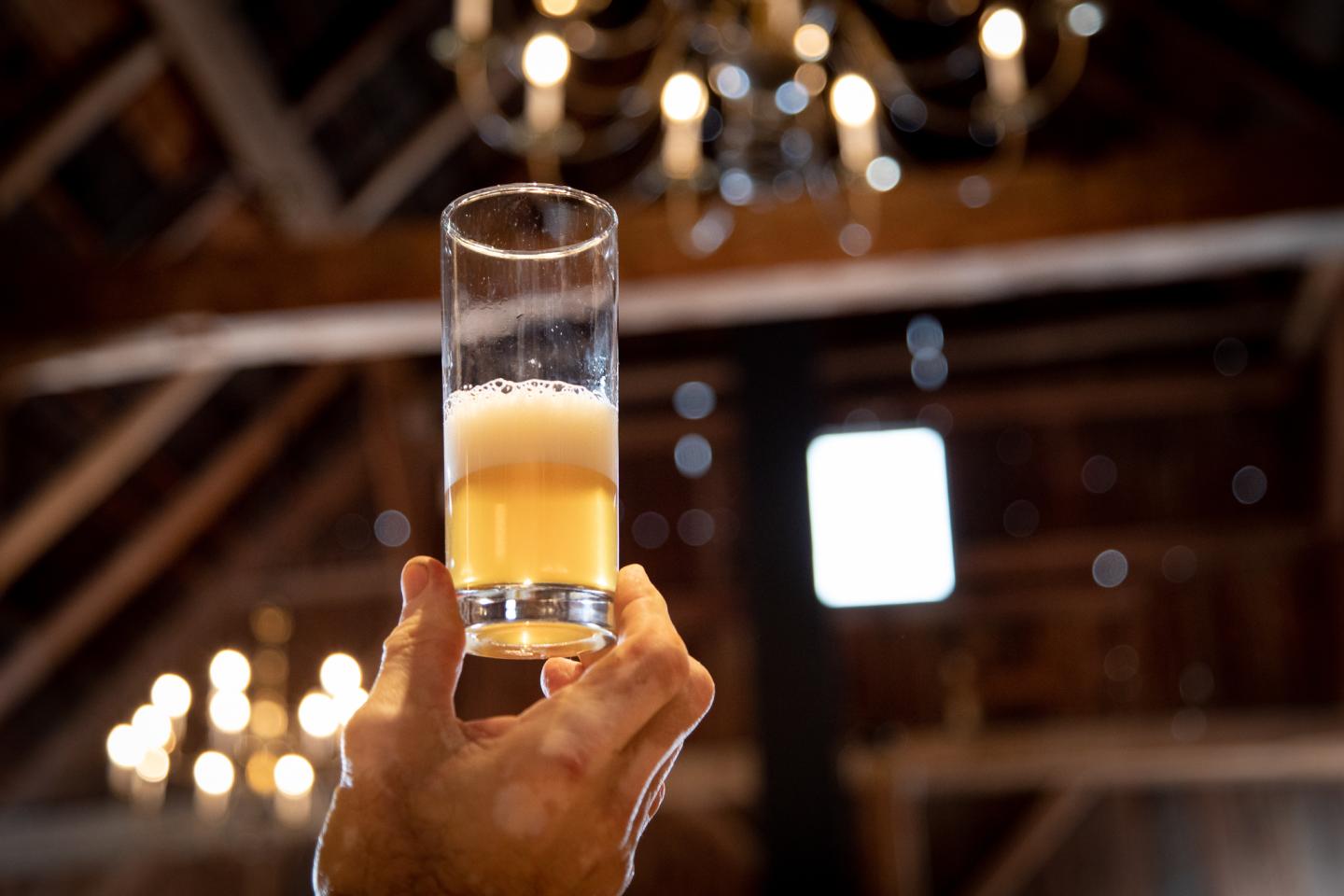Hand holding a half-full beer glass in a rustic setting with chandeliers.