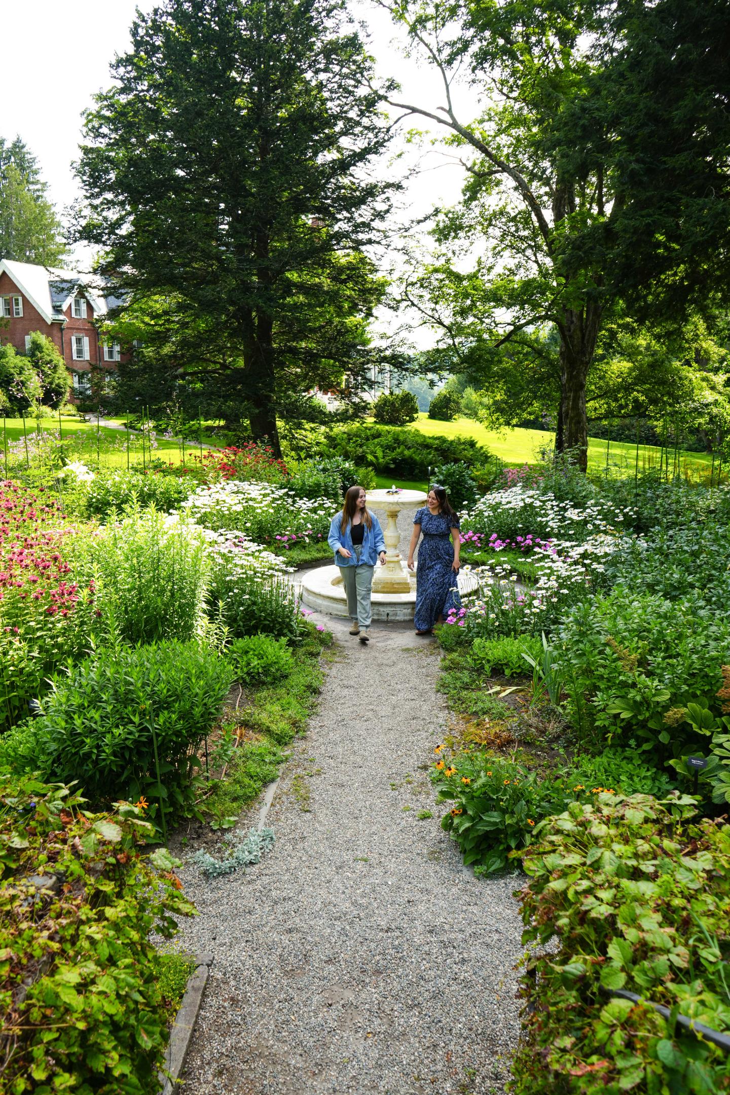 Garden path with two people, surrounded by lush greenery and flowers.