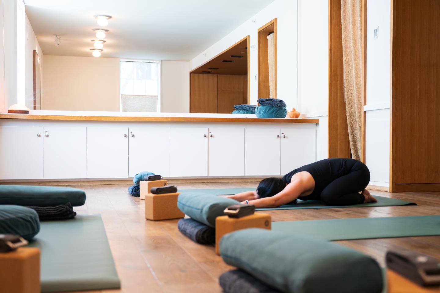 Person in child's pose on yoga mat in a well-lit studio.