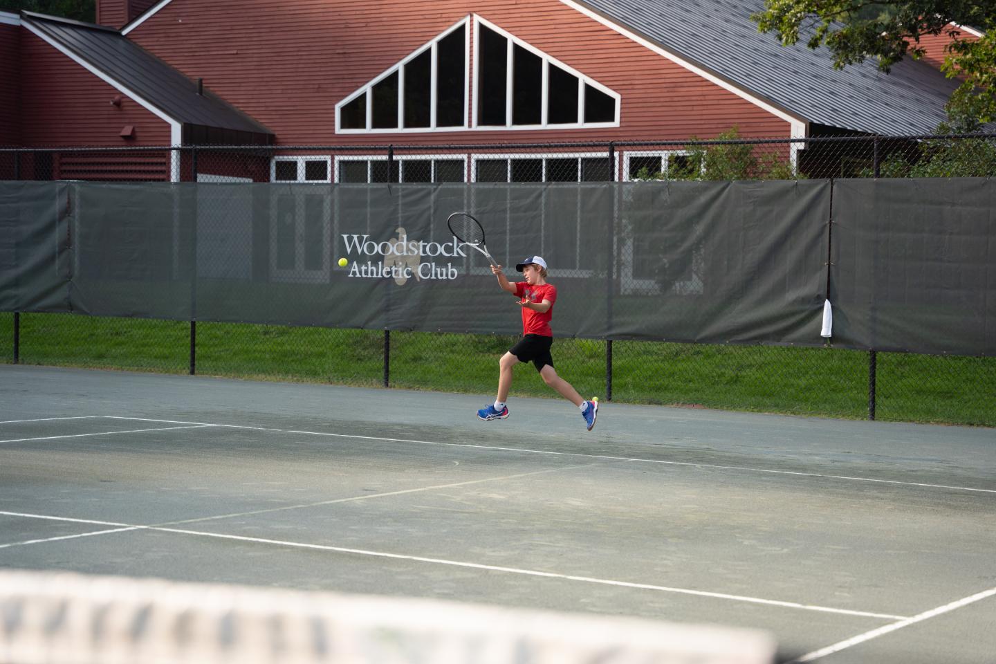Tennis player in red shirt jumps for a shot on an outdoor court.