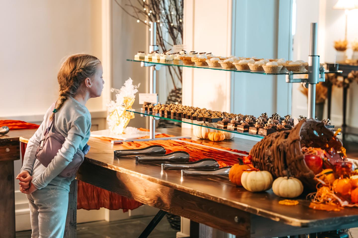 Child gazing at a dessert table with pastries and autumn decorations.