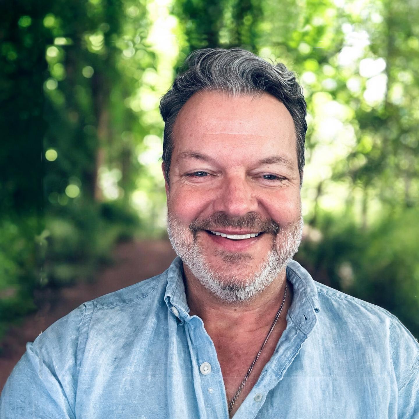 Richard Enderlin wearing a blue shirt with lush green background.