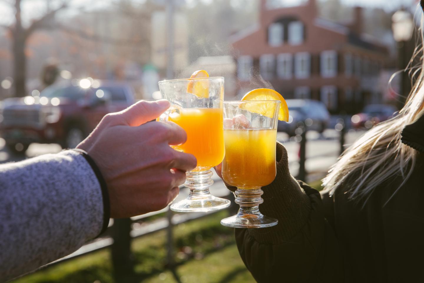 Hands clinking glasses of orange juice outdoors.