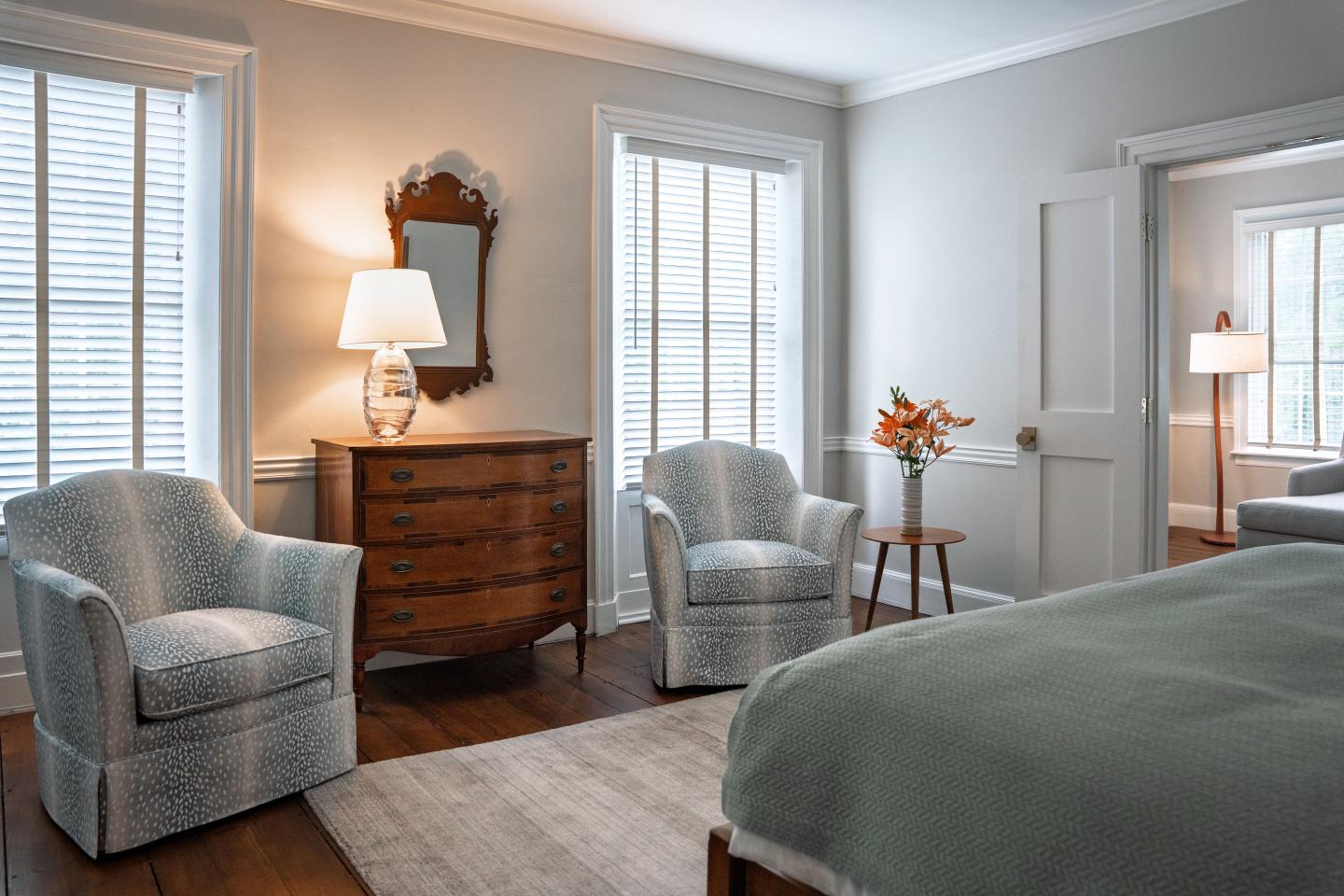 Cozy bedroom with armchairs, dresser, and a neatly made bed in soft gray tones.