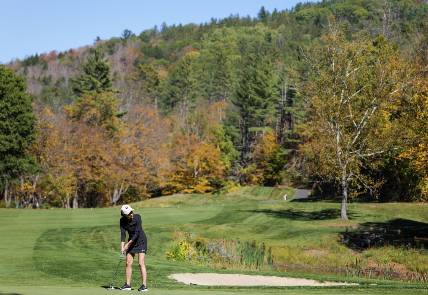 Golfer putting on a green surrounded by autumn trees.