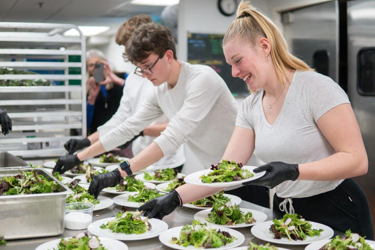 Two members of Change The World Kids plating salads in a commercial kitchen.