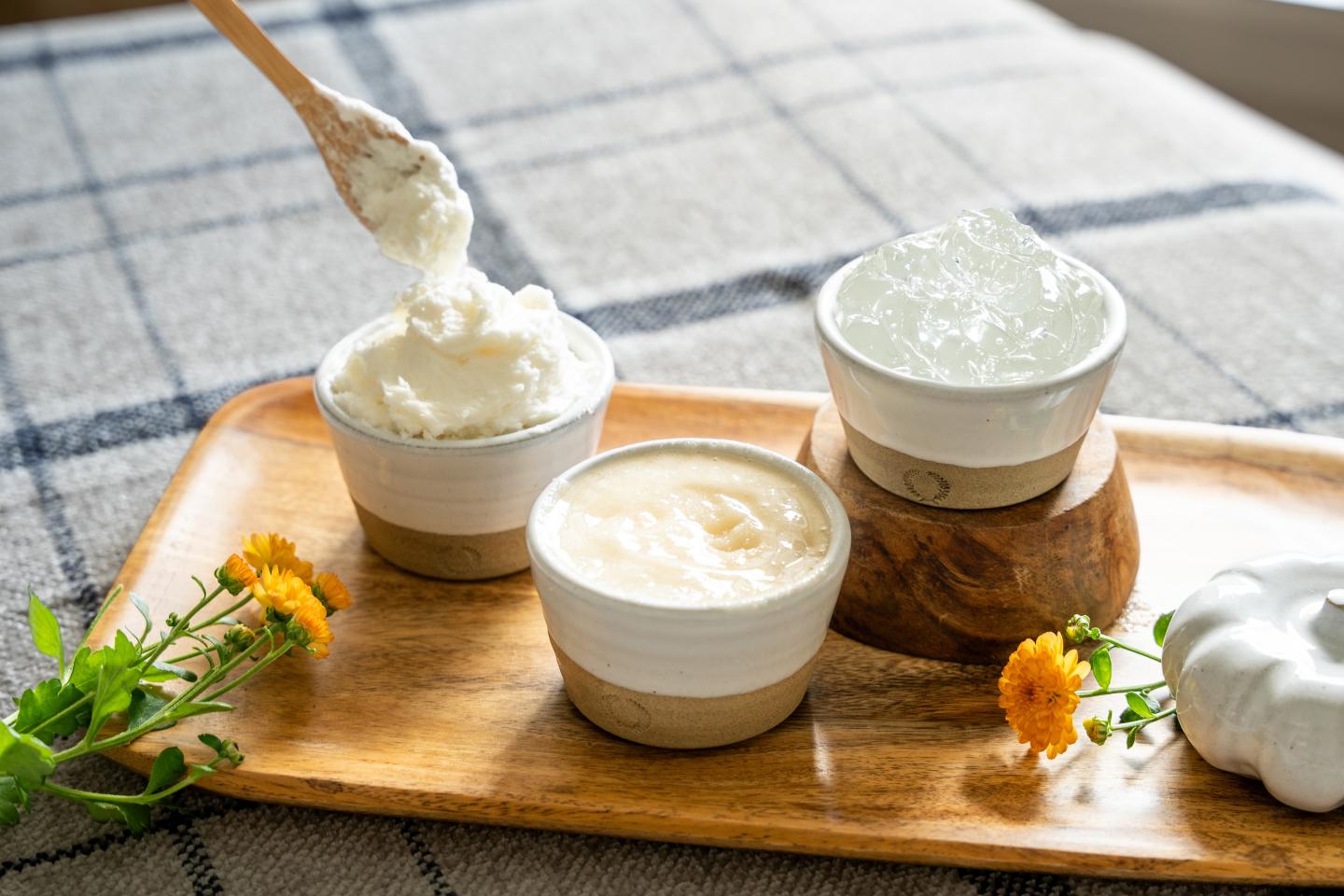 Three bowls of creamy yogurt on a wooden board, with honey and flowers.