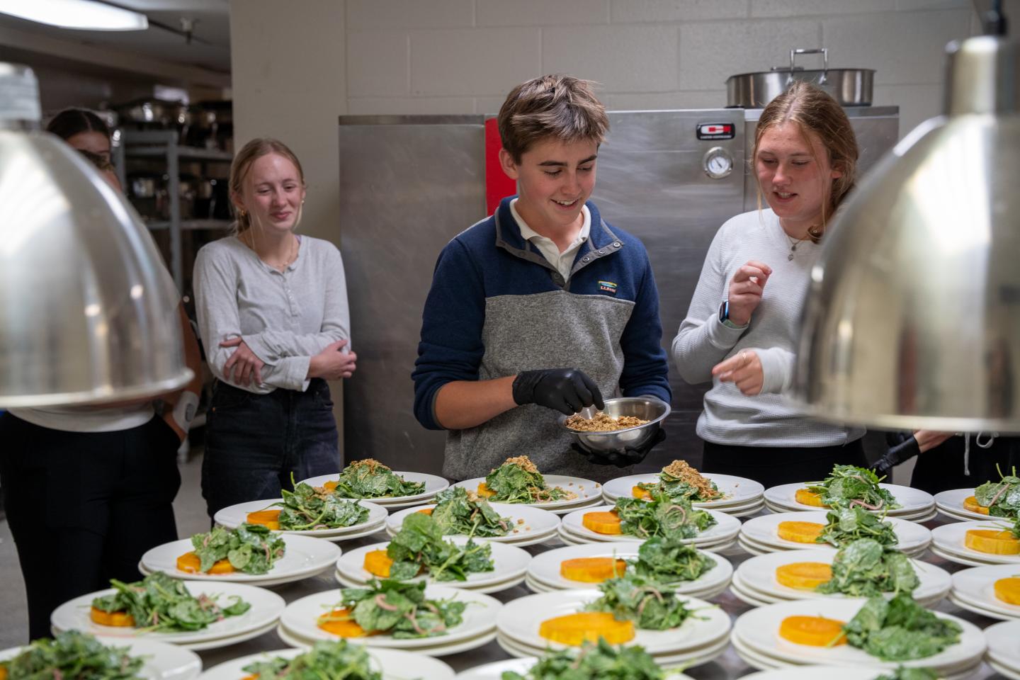 Chefs plating green and orange appetizers in a busy professional kitchen.