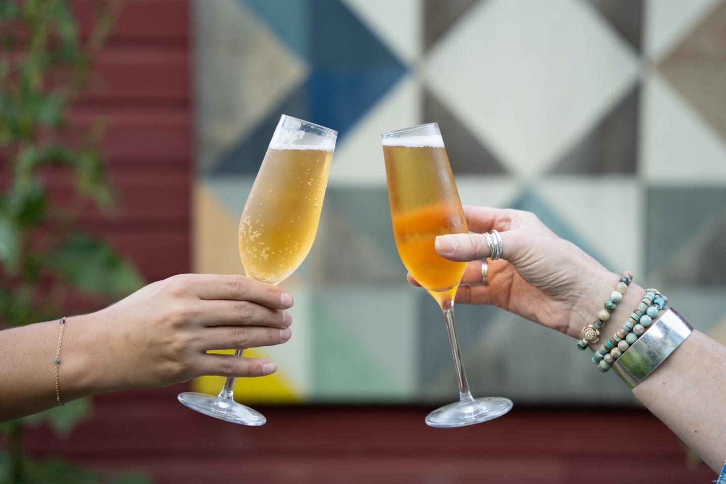 Two people clinking champagne flutes against a geometric mural.
