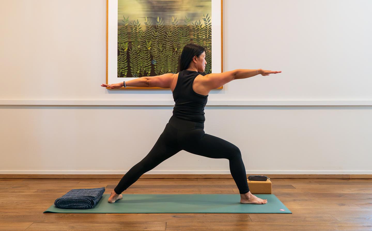 Woman practicing Warrior II yoga pose on a mat in wellness studio.