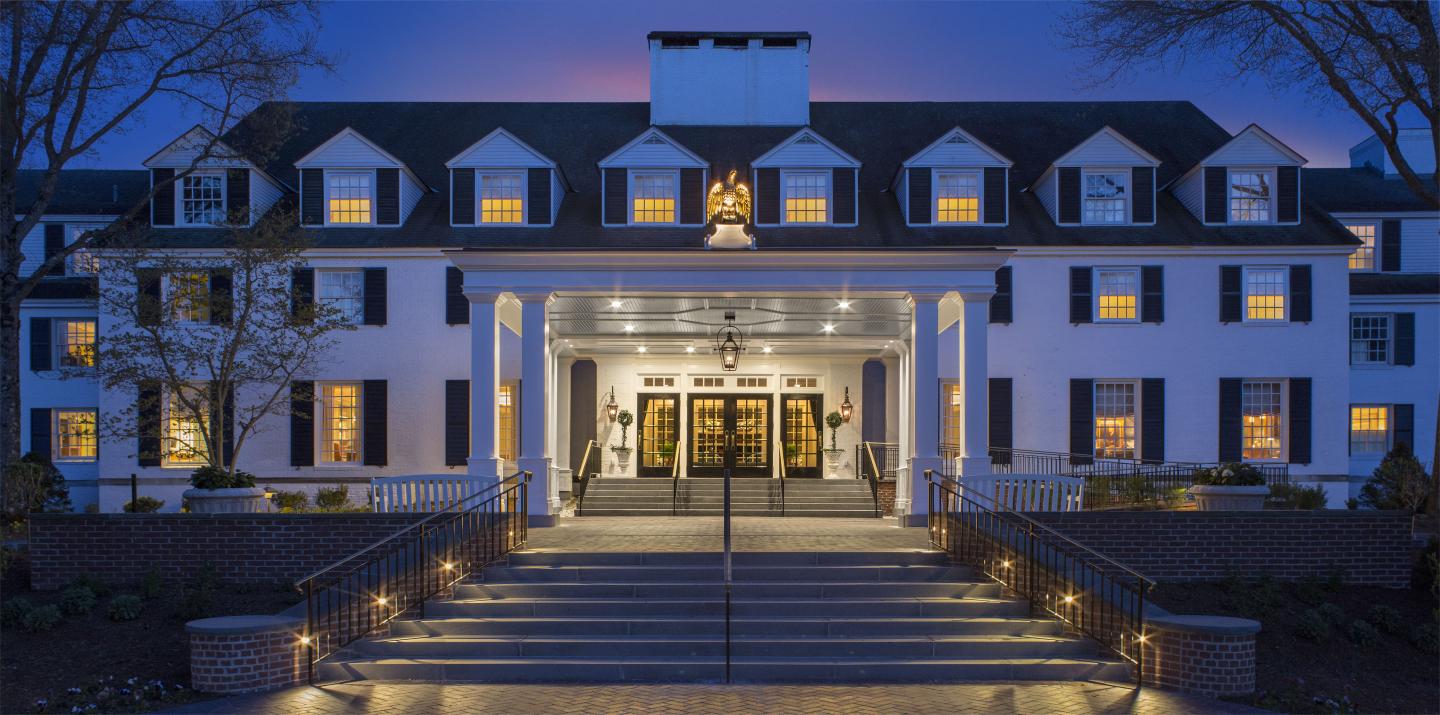 Grand, illuminated white mansion at dusk with a wide staircase and glowing entrance.